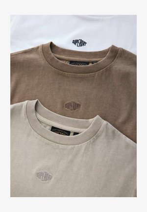 Tri kratke majice hrptene: jedna bijela, jedna tamnosmeđa i jedna svijetlobéž. Svaka ima rebrasti izrez i izvezeni logotip.