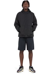 Sort hættetrøje med lynlås, to frontlommer, parret med mørke shorts og multicolore sneakers. Letvægtsmateriale, afslappet pasform.