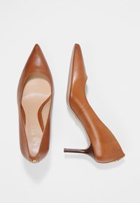 Bruna läder högklackade pumps med spetsig tå, slät yta och smal klack. Innersulan visar en ljus beige färg.