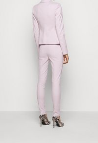 Vaaleanpunainen räätälöity puku, jossa on istuva bleiseri ja kapeat housut, yhdistettynä musta-valkoisiin käärmeennahkakuosiset korkokenkiin.