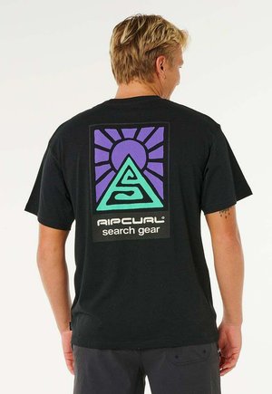 Uomo che indossa una maglietta nera con un design colorato di montagne geometriche e sole e la scritta "Rip Curl search gear" sul retro.