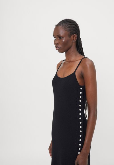 Schwarzes gestricktes Kleid mit dünnen Trägern, das auf der Seite mit runden Knöpfen versehen ist und eine figurbetonte Silhouette hat. Glatte Textur und minimalistisches Design.