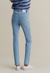 Jean slim bleu clair en denim, avec deux poches arrière et une étiquette de ceinture simple, porté avec des baskets blanches.