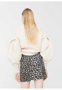 Suéter de color crema oversize con mangas abullonadas, combinado con una falda corta de estampado de leopardo en blanco y negro, mostrado desde la parte de atrás.