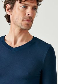 Maglietta a maniche lunghe blu navy con scollo a V, realizzata in un tessuto morbido e testurizzato con un design aderente che mette in risalto il torso e l'area del collo.