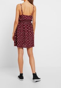 Burgundy klänning med små vita blommotiv, elastisk midja och tunna remmar. Avslutad med en utsvängd kjol. Bärs med svarta högskor.