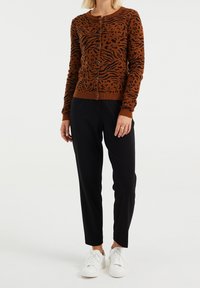 Brun cardigan med svart djurmönster, långa ärmar, rund halsringning och knappstängning, i kombination med svarta byxor och vita sneakers.