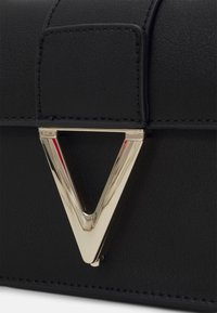 Borsa a tracolla in pelle nera con un accento hardware triangolare dorato, texture liscia e dettaglio di cucitura a contrasto sulla patta.