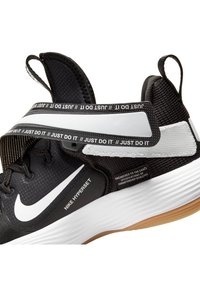 Scarpa atletica nera con tomaia testurizzata, logo Nike Swoosh bianco e fascia "Just Do It". Suola in gomma con scanalature e fondo beige.