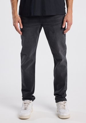 Zwarte denim jeans met een slim fit. Ze hebben een klassiek vijf-pocket ontwerp en subtiele vervaging, gecombineerd met witte sneakers.