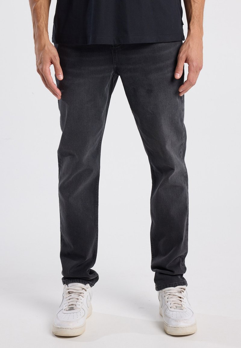 Vaqueros de mezclilla negros de corte slim. Tienen un diseño clásico de cinco bolsillos y un ligero desgaste, combinados con zapatillas blancas.