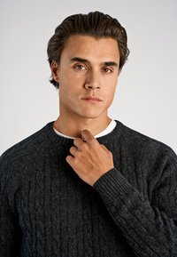 Ciemnoszary sweter z dzianiny warkoczowej z okrągłym dekoltem. Materiał wydaje się miękki i teksturowany, z prążkowanymi mankietami i klasycznym krojem.