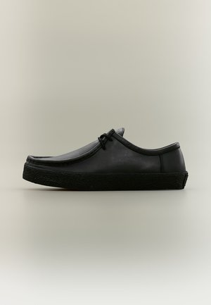 Chaussure basse en cuir noir avec semelle épaisse texturée et lacets noirs, présentée de profil sur fond neutre.
