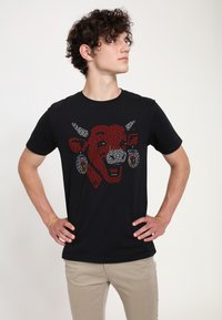 Schwarzes Baumwoll-T-Shirt mit einem roten und weißen Grafikmotiv eines Kuhkopfes mit Ohrringen, klassischer Rundhalsausschnitt, kurze Ärmel und lässige Passform.