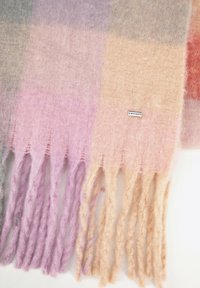 Wełniany szalik z pastelowym wzorem w blokowe kolory w odcieniach szarości, różu i brzoskwini; zakończony frędzlami; widoczna mała metka z logo.