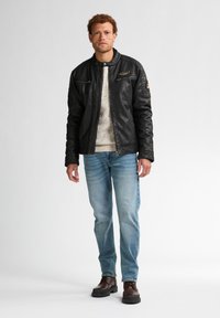 Chaqueta de cuero negra con cremallera y cuello a presión, combinada con un suéter ligero, jeans azules y botas marrones con cordones.
