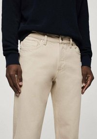 Vaqueros de algodón beige con un diseño de pierna recta. Presentan bolsillos frontales, una cremallera en la bragueta y detalles de costura sutiles.
