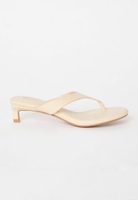 Beige klacksandaler med en minimalistisk design, som har en bred rem och tåpost. Slät textur och en kort blockklack för stabilitet.