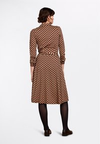 Vestito marrone con colletto e maniche lunghe, caratterizzato da un motivo floreale in crema e rosso. Include una vita svasata e una gonna a ruota.
