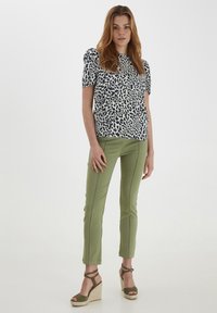 Top a maniche corte bianco con stampa animale nera, abbinato a pantaloni verdi oliva aderenti, con cuciture a contrasto e sandali con zeppa piatta.