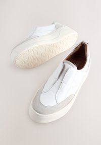 Zapatos sin cordones de cuero blanco con detalles en ante gris y suelas de goma texturizadas. Presentan un acabado liso y paneles laterales elásticos para fácil uso.