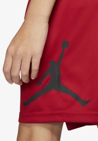 Czerwone siatkowe spodenki do koszykówki z czarnym sylwetkowym logo Air Jordan na dolnej lewej stronie. Gładka tekstura z luźnym krojem.