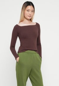 Top marrón de manga larga con textura de canalé y escote cuadrado, combinado con pantalones verdes tipo tapered que cuentan con bolsillos laterales y un ajuste relajado.