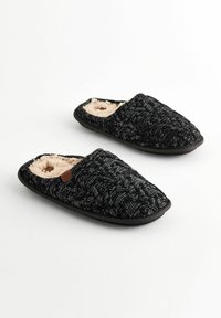Black knitted slippers with a textured pattern and plush beige lining. The sole is flat and black, designed for indoor use.