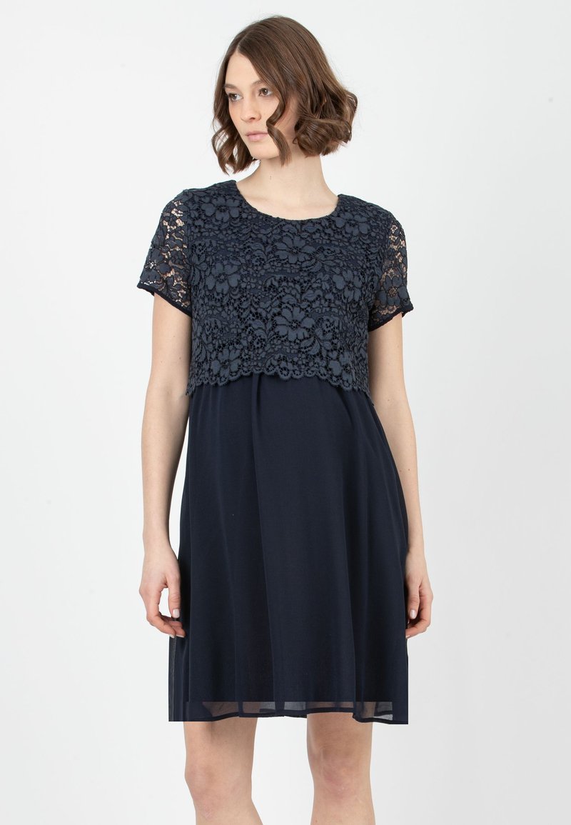 Kneehoher navyblauer Kleid mit einem Spitzenoverlay-Oberteil, kurzen Ärmeln und einem schwingenden Rock. Die Spitze weist florale Muster mit gewellten Kanten auf.