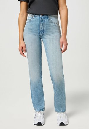 Light blue high-waisted jeans with a straight leg design, featuring a faded texture and subtle stitching details, paired with white sneakers.