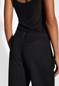 Zwarte, geribbelde stoffen broek met een subtiele glans, achterzakken en een getailleerde pasvorm, de weergave richt zich op de taille en het achterontwerp.