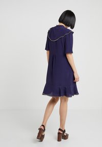 Mörkblå klänning med korta ärmar, volangkant och kontrasterande kanter på kragen. Slät tyg med en utsvängd siluett.