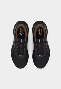 Ζευγάρι μαύρα αθλητικά παπούτσια Asics με καφέ εσωτερικό, κόκκινους βρόχους για τα κορδόνια και ετικέτα Gore-Tex, απεικονιζόμενα από πάνω σε λευκό φόντο.