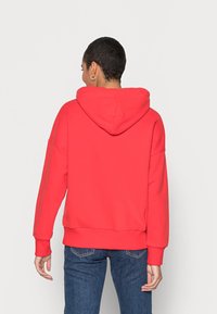 Rood hoodie met een losse pasvorm, ribgebreide manchetten en onderrand, met een gladde textuur. Draagt met blauwe spijkerbroek.