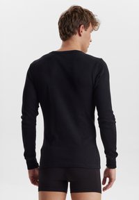 Schwarzes Langarmshirt aus einem weichen Stoff, mit rundem Halsausschnitt und eng anliegenden Ärmeln, glatter Textur und minimalistischem Design.