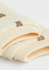 Cremefarvede strikkede sokker med let ribbede detaljer og et mønster af brune bjørne over det hele. Stofferne er bløde og hyggelige.