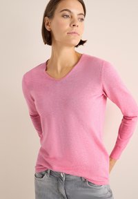 Roze langharige trui met een V-hals ontwerp, gemaakt van een glad gebreide stof, met subtiele textuur en aansluitende mouwen.