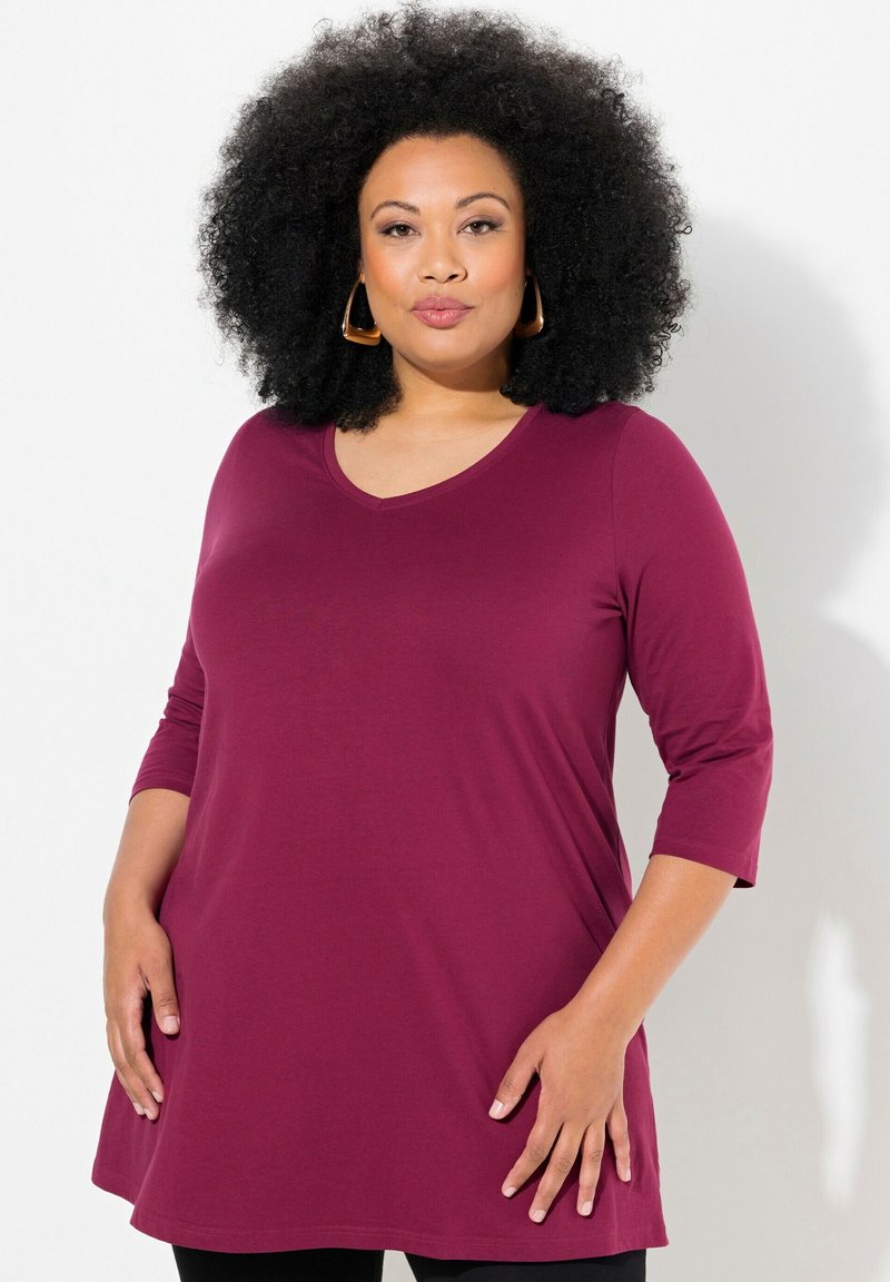 Camicia tunica a maniche lunghe bordeaux con scollatura a V, morbido al tatto e dal fit fluido, abbinata a pantaloni neri aderenti.