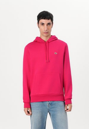 Hoodie roz strălucitor cu o buzunar tip cangur, glugă cu șnur, mansete cu dantelă și un mic logo verde Lacoste pe piept.
