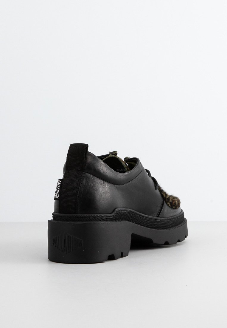 Chaussure en cuir noir avec une semelle en caoutchouc noir épaisse, présentant un accent texturé et un patch logo sur le talon.