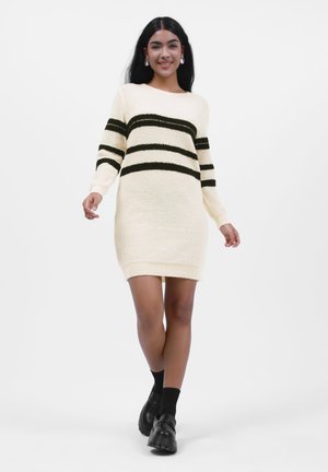 Robe pull couleur crème avec des rayures horizontales noires, des poignets côtelés et une coupe décontractée, fabriquée à partir d'un tissu doux et texturé.