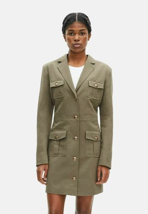 Olijfgroene blazer jurk van gladde stof, met twee borstzakken, twee voorzakken en grote gouden knopen accenten.