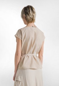 Beige, let bluse med rund halsudskæring, korte ærmer og bindebånd i taljen. Glat tekstur og løs pasform.