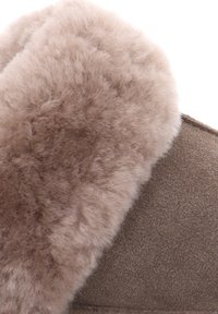 Braune Wildlederschlappen mit einem weichen, strukturierten, hellbraunen Kunstfellfutter entlang der Öffnung. Abgerundetes Design für Komfort und Wärme.