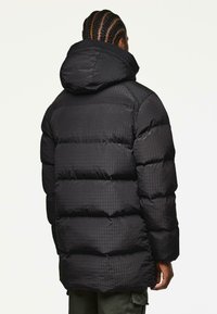 Schwarze Pufferjacke mit gestepptem Muster, ausgestattet mit einer Kapuze und einer langen Silhouette. Der Stoff hat einen leichten Glanz und ist isoliert.