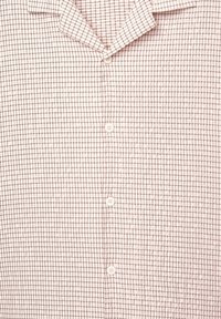 Chemise blanche boutonnée avec un petit motif en grille noire et un col, montrée de la poitrine jusqu'à la taille.