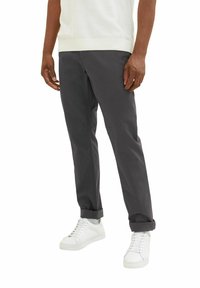 Graue Chinos mit geradem Schnitt, mit umgeschlagenen Säumen und Seitentaschen, kombiniert mit weißen Sneakers. Glatte Baumwollstofftextur.