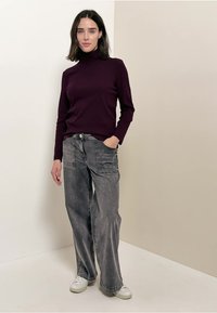 Bordeauxfarbener Rollkragenpullover kombiniert mit lockeren, grauen, verwaschenen Cargo-Hosen und weißen Sneakers. Einfaches Design mit minimalen Akzenten.