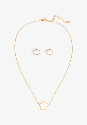 Goldene Halskette und passende Ohrstecker mit weißen, blumenförmigen Anhängern vor weißem Hintergrund.