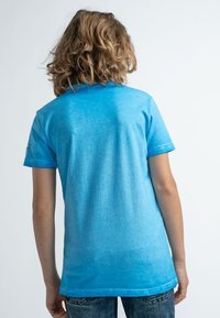 Ljusblå bomullströja med avslappnad passform, korta ärmar och en något blekt textur. Har en sydd fåll och en avslappnad design.